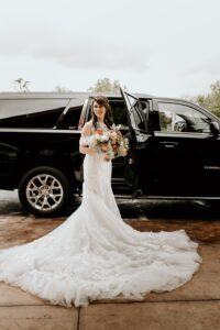 bride posing with bouquet by black car